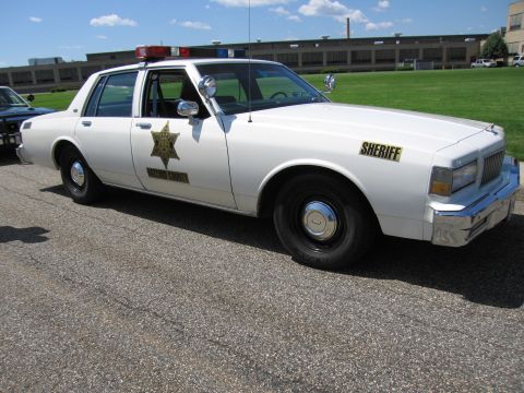 1991 Ford LTD Crown Victoria - white 1980s Chevrolet Caprice sheriff cruiser with a gold star door emblem, SHERIFF lettering and roof beacons.