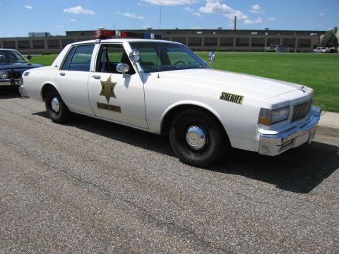 1991 Ford LTD Crown Victoria - Front three-quarter view of a white Chevrolet Caprice sheriff cruiser with gold star emblem and SHERIFF lettering.
