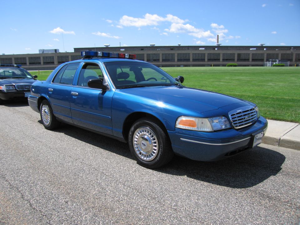 Blue Ford Crown Victoria police sedan with roof light bar on pavement