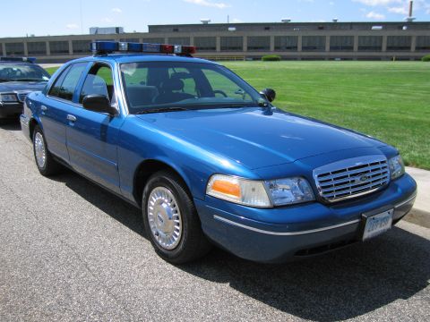 1991 Ford LTD Crown Victoria - Front three-quarter view of a blue Ford Crown Victoria police sedan with red-and-blue roof light bar parked on a road.