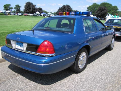1991 Ford LTD Crown Victoria - Rear three-quarter view of a blue Ford Crown Victoria police sedan with roof light bar at an outdoor vehicle show.
