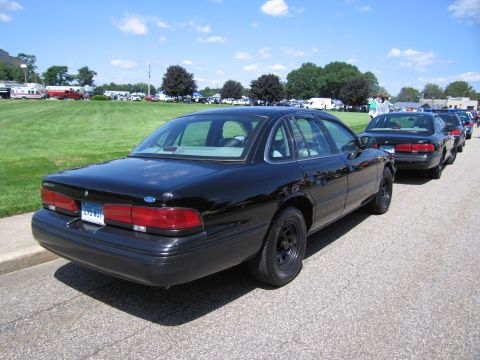 1991 Ford LTD Crown Victoria - Rear three-quarter view of a black Ford sedan parked in a row of vehicles at a grassy outdoor car show.