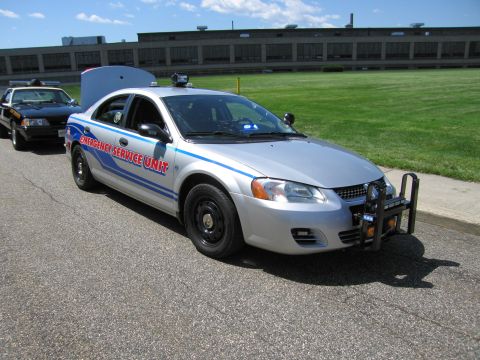 1991 Ford LTD Crown Victoria - silver Dodge sedan marked 'Emergency Service Unit' with blue striping and a front push bar parked near a green field.