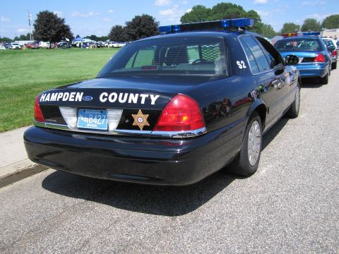 1991 Ford LTD Crown Victoria - Rear three-quarter view of a black Ford Crown Victoria marked 'Hampden County' with a gold star and roof light bar at a show.