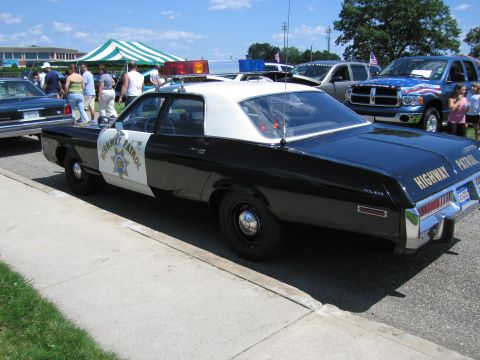 1991 Ford LTD Crown Victoria - black-and-white Highway Patrol two-door sedan with a gold star emblem and roof lights parked at a crowded outdoor show.