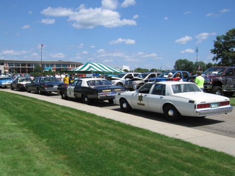 1991 Ford LTD Crown Victoria - long row of classic police cars including a Highway Patrol sedan and a white star-marked sheriff sedan at an outdoor show.