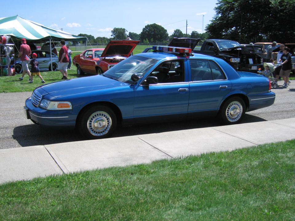 Blue Ford Crown Victoria police sedan with light bar parked by tents