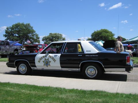1991 Ford LTD Crown Victoria - black-over-white California Highway Patrol sedan with star door shield parked on pavement at an outdoor car show.