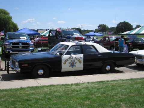 1991 Ford LTD Crown Victoria - black-and-white Highway Patrol cruiser with white roof and star door emblem parked at a car show with vehicles behind.