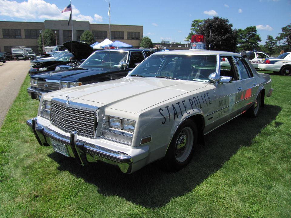 Silver Chrysler State Police sedan with red stripe and light bar on grass