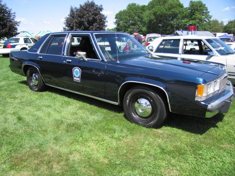 1991 Ford LTD Crown Victoria - dark-blue full-size Ford police sedan with door emblem and steel wheels parked on grass among other cruisers.