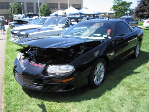 1991 Ford LTD Crown Victoria - black Chevrolet Camaro coupe with its hood raised, parked on grass among other vehicles at an outdoor car show.