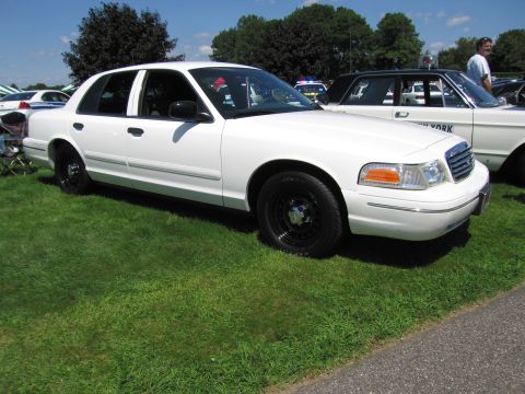 1991 Ford LTD Crown Victoria - white Ford Crown Victoria police sedan with black steel wheels parked on grass beside other cruisers at a car show.