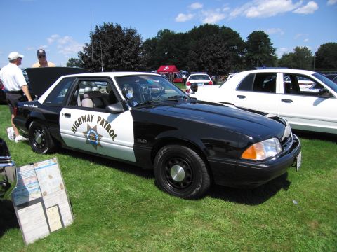 1991 Ford LTD Crown Victoria - black-and-white Highway Patrol Ford Mustang 5.0 coupe with star door emblem parked on grass at a car show.