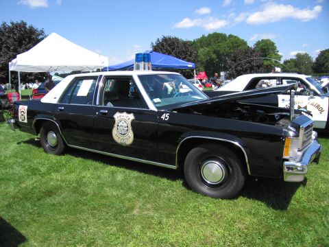 1991 Ford LTD Crown Victoria - black-and-white Ford Crown Victoria police sedan marked 45 with door badge parked on grass at an outdoor car show.