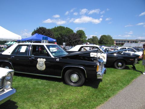 1991 Ford LTD Crown Victoria - black-and-white police sedan marked 45 with door badge displayed in a row of cruisers on grass at a car show.