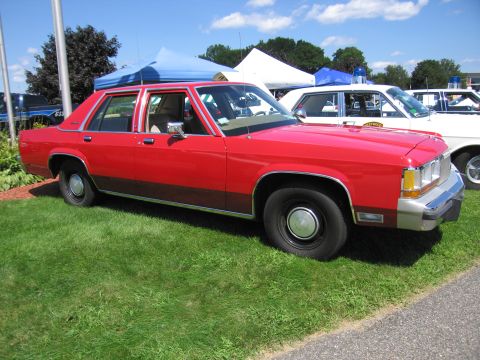 1991 Ford LTD Crown Victoria - red four-door Ford LTD Crown Victoria sedan with wood-grain side trim sits on grass at an outdoor car show.