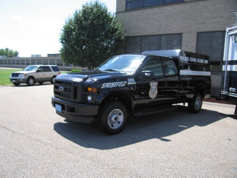 1991 Ford LTD Crown Victoria - black Ford F-250 Super Duty Springfield police crime-scene-unit pickup with a covered bed parked outside a brick building.
