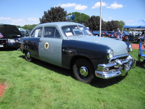 1991 Ford LTD Crown Victoria - restored early-1950s Ford two-tone gray state police sedan with a roof beacon parked on grass at an outdoor show.