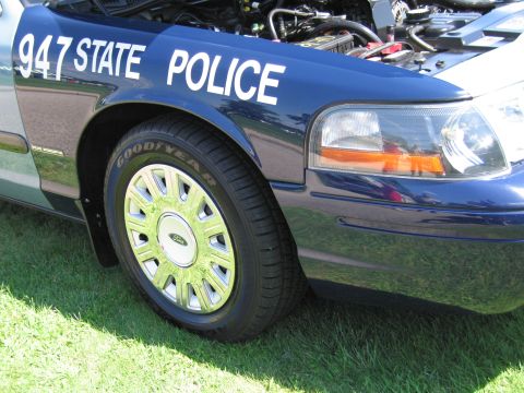 1991 Ford LTD Crown Victoria - Close-up of the front fender of a dark-blue '947 State Police' cruiser, showing the headlight, Goodyear tire and Ford hubcap.