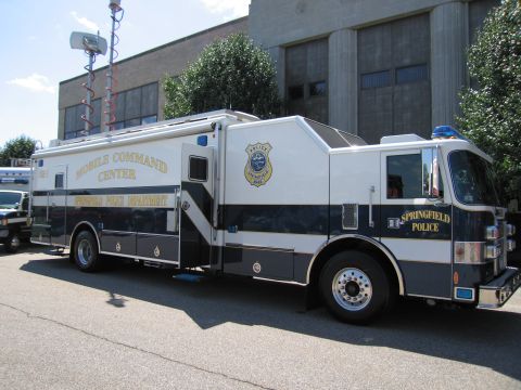 1991 Ford LTD Crown Victoria - white-and-blue Springfield Police 'Mobile Command Center' truck with a raised mast antenna parked beside a building.