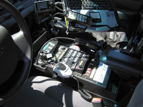 1991 Ford LTD Crown Victoria - cluttered front interior of a police cruiser with steering wheel, two-way radios, control console and a mounted laptop.