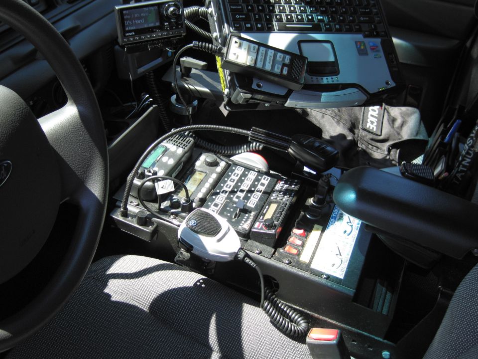 Police cruiser interior showing steering wheel, radios, laptop mount and console controls