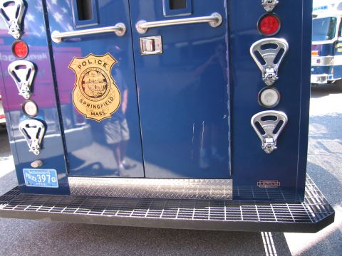 1991 Ford LTD Crown Victoria - Lower rear of a blue Springfield, Mass police armored truck showing a gold badge decal, lights and a diamond-plate step bumper.