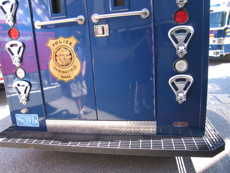Lower rear of a blue Springfield police armored truck with gold badge and diamond-plate step