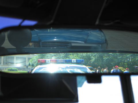 1991 Ford LTD Crown Victoria - Looking out a windshield at a police car with an illuminated red and blue light bar, with crowds and trees beyond.