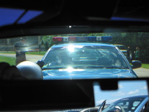 1991 Ford LTD Crown Victoria - blue police car marked State Police with a roof light bar, seen through the windshield of another car on a sunny day.