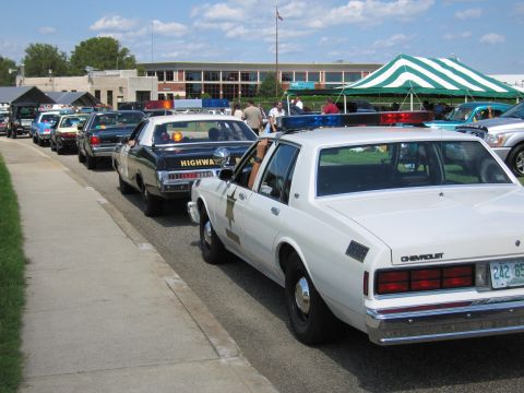 1991 Ford LTD Crown Victoria - white Chevrolet police cruiser and a black Highway Patrol sedan parked in a row at an outdoor car show.