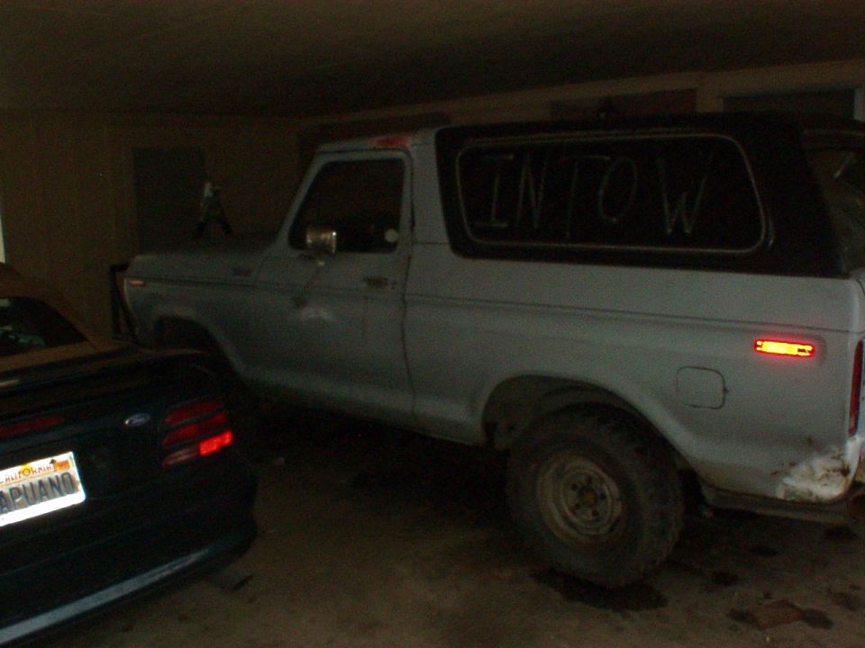 Light blue Ford Bronco parked in garage with 'INTOW' on rear window, dark convertible at left