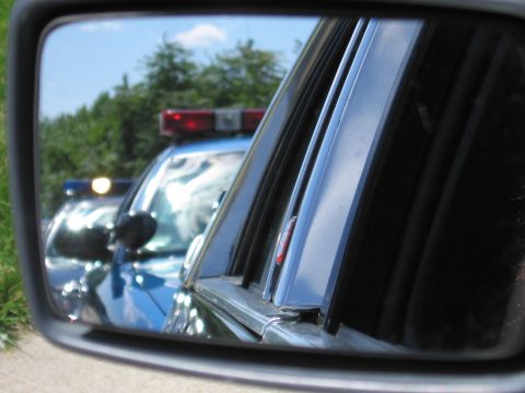 1991 Ford LTD Crown Victoria - car's side mirror reflects a blue police car with a roof light bar parked on a grassy roadside.