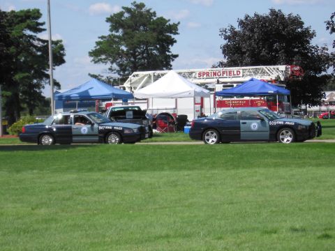 1991 Ford LTD Crown Victoria - Two State Police cars, a sedan and a Charger, parked on grass beside tents with a Springfield fire ladder behind.