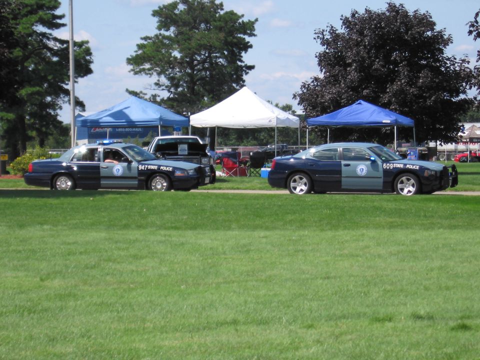 State Police sedan and Dodge Charger cruiser parked on grass by tents