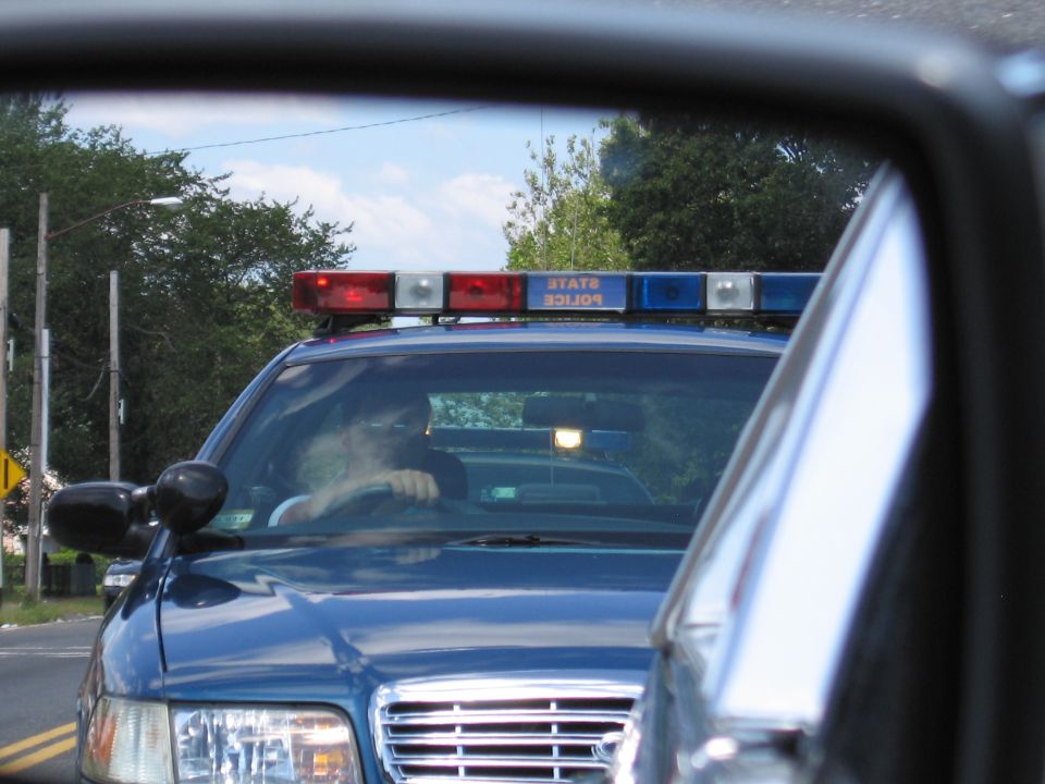 Blue State Police Ford with lit light bar viewed through a car window