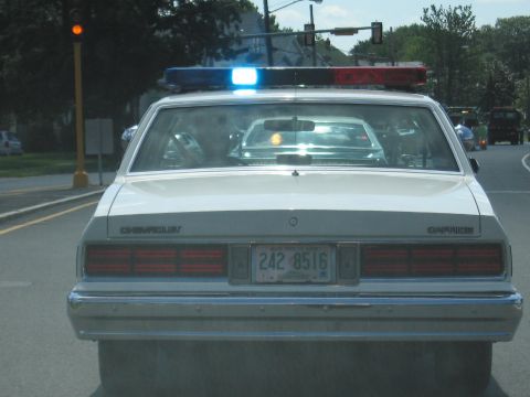 1991 Ford LTD Crown Victoria - rear of a white Chevrolet Caprice police car with an illuminated light bar stopped on a street at a light.