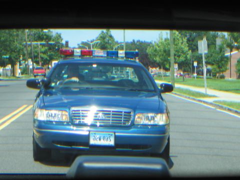 1991 Ford LTD Crown Victoria - blue Ford police car with a roof light bar on a road, viewed through the windshield of another vehicle.