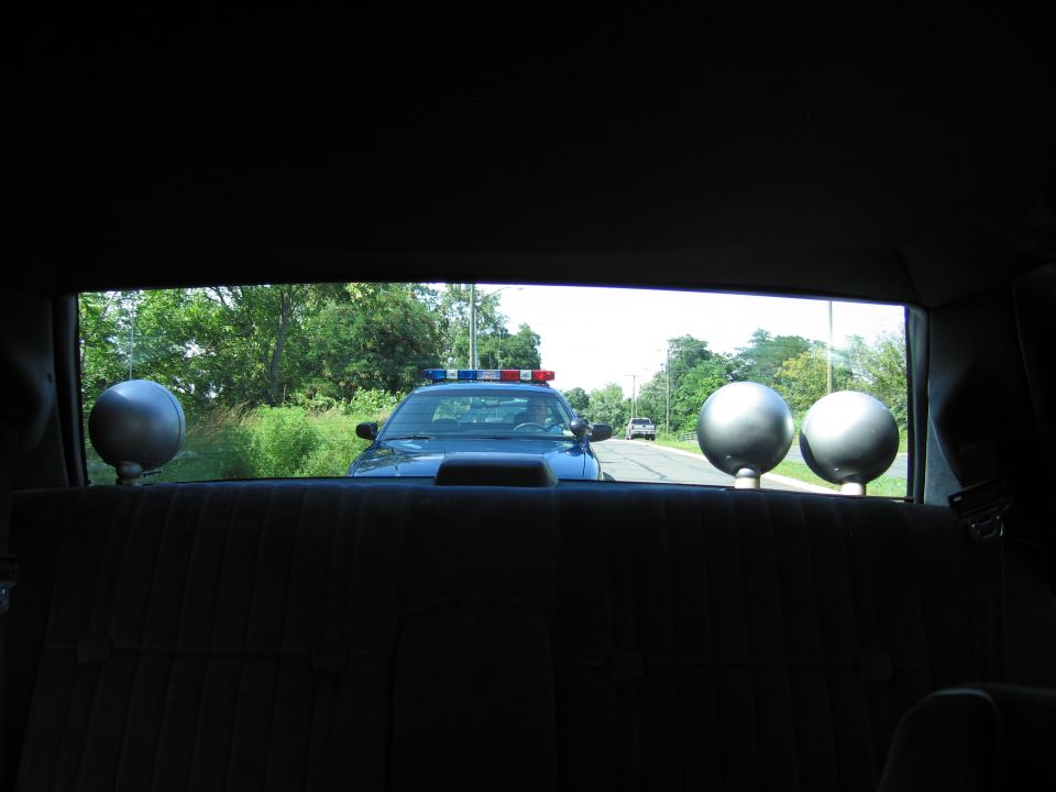 View from a car back seat through rear window at a blue police car following