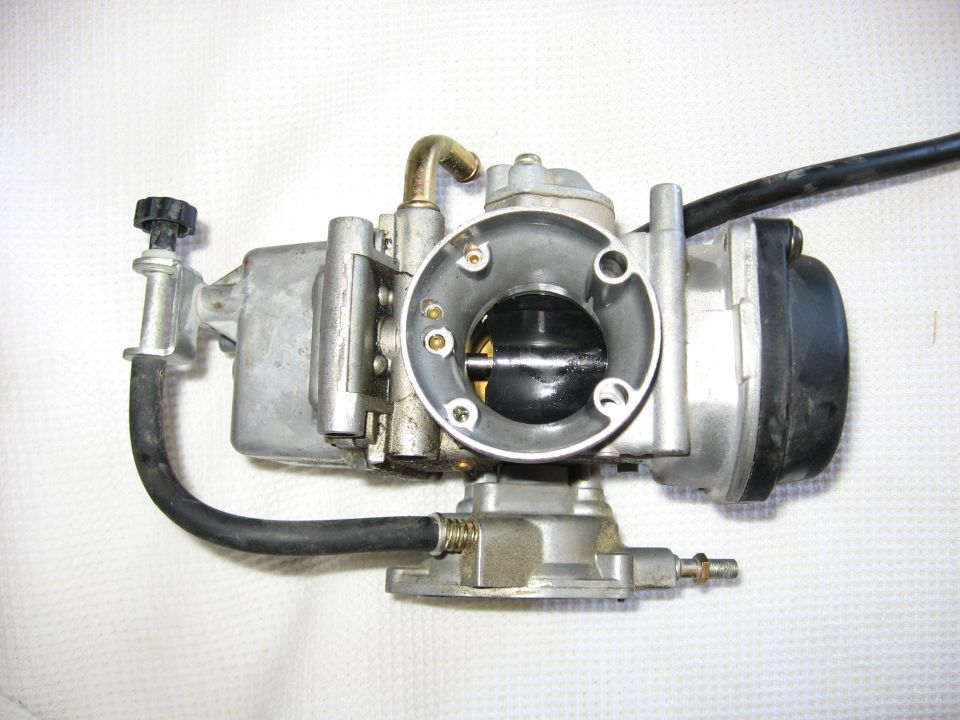 Carburetor with black hoses and brass fittings, viewed from the side