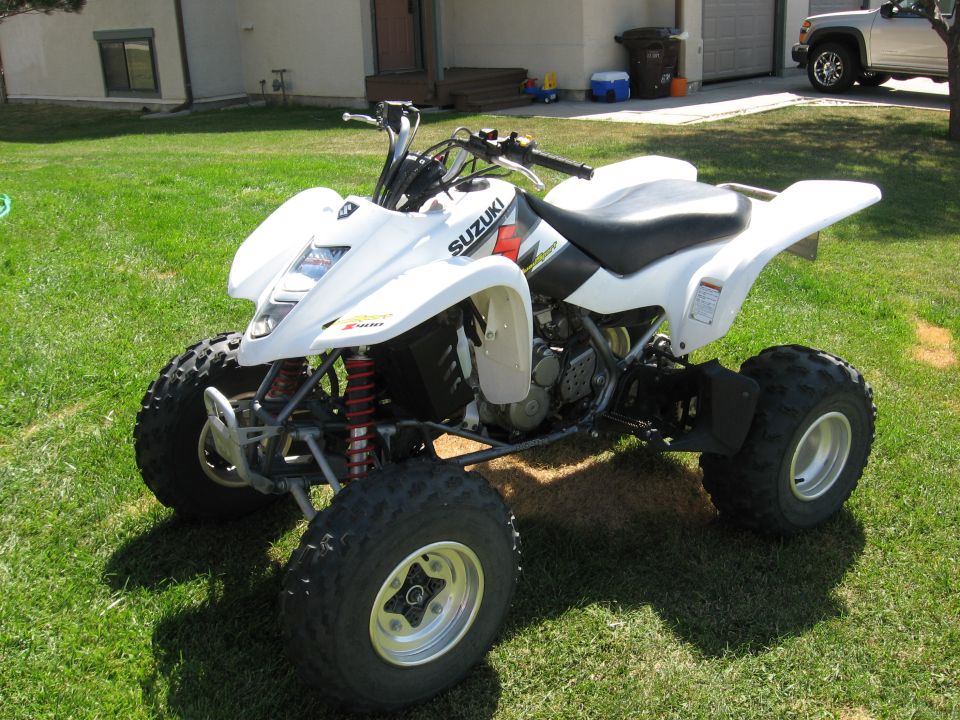 White Suzuki sport ATV quad parked on grass by a driveway