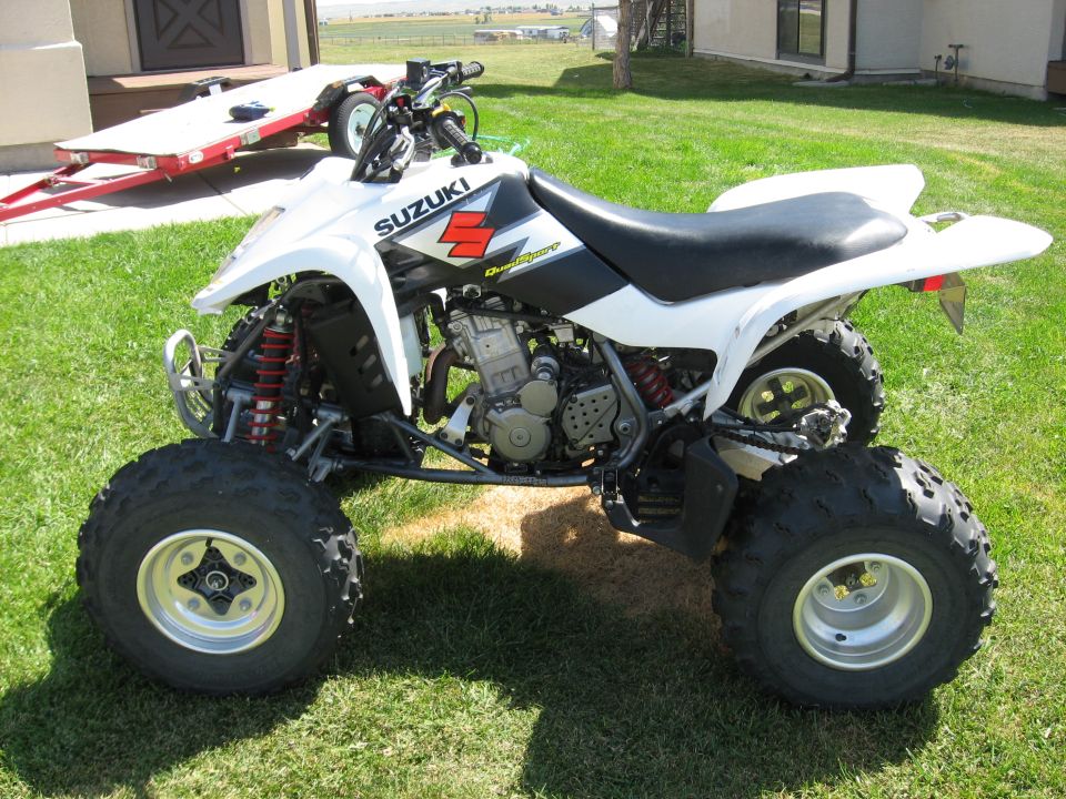White Suzuki quad bike parked on grass with a trailer behind it