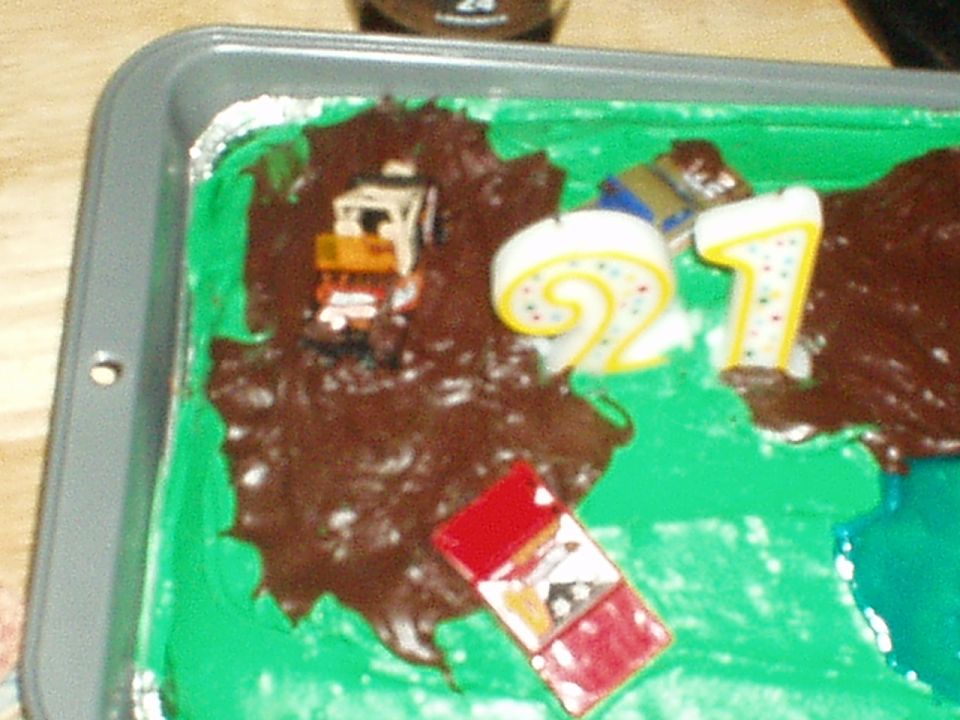 Birthday cake with green icing, chocolate 'mud', toy truck, and 21 candles