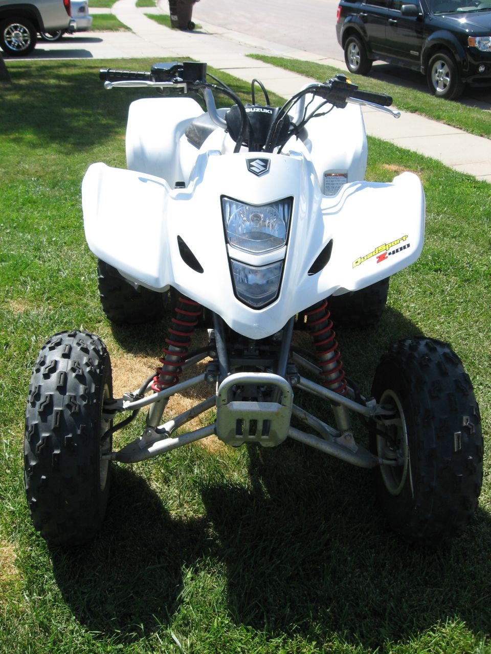 White sport ATV parked on a lawn, front view with Suzuki badge