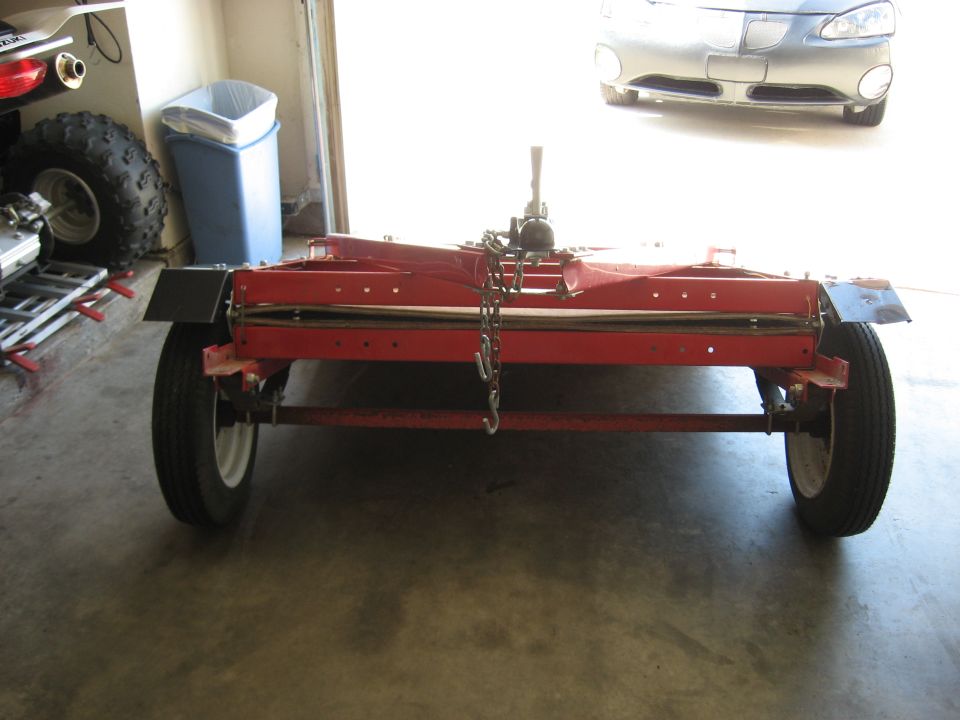 Red folding utility trailer with wheels and chains inside a garage