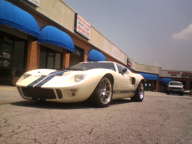 Cream GT40-style coupe with black stripes and polished wheels parked outside shops