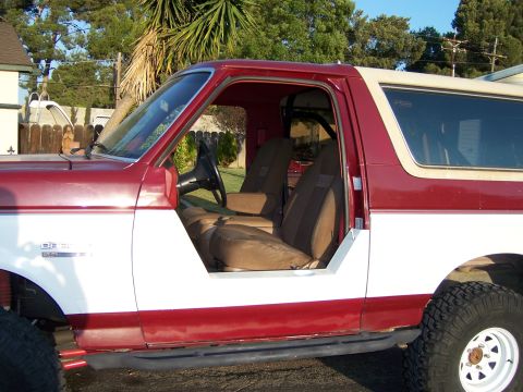 1991 Ford Bronco - The side profile of a two-tone Ford Bronco, its interior with tan seats and a roll cage.
