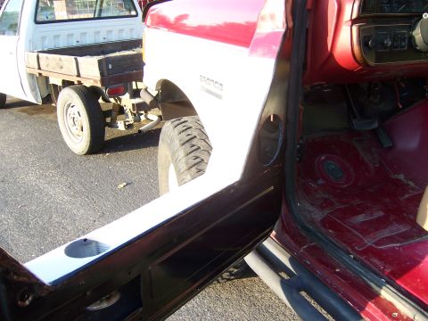 1991 Ford Bronco - Interior view of a red 1991 Ford Bronco with the driver's door open, revealing the dashboard and floor. A white flatbed truck is parked beh…