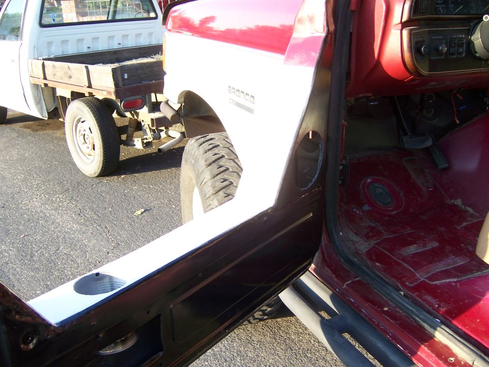 Red 1991 Ford Bronco interior with door open, showing dashboard and floor. Another white truck is visible in the background